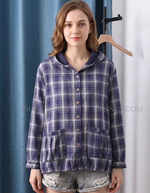 Woman wearing a blue plaid shirt with a hood in front of a blue curtain.