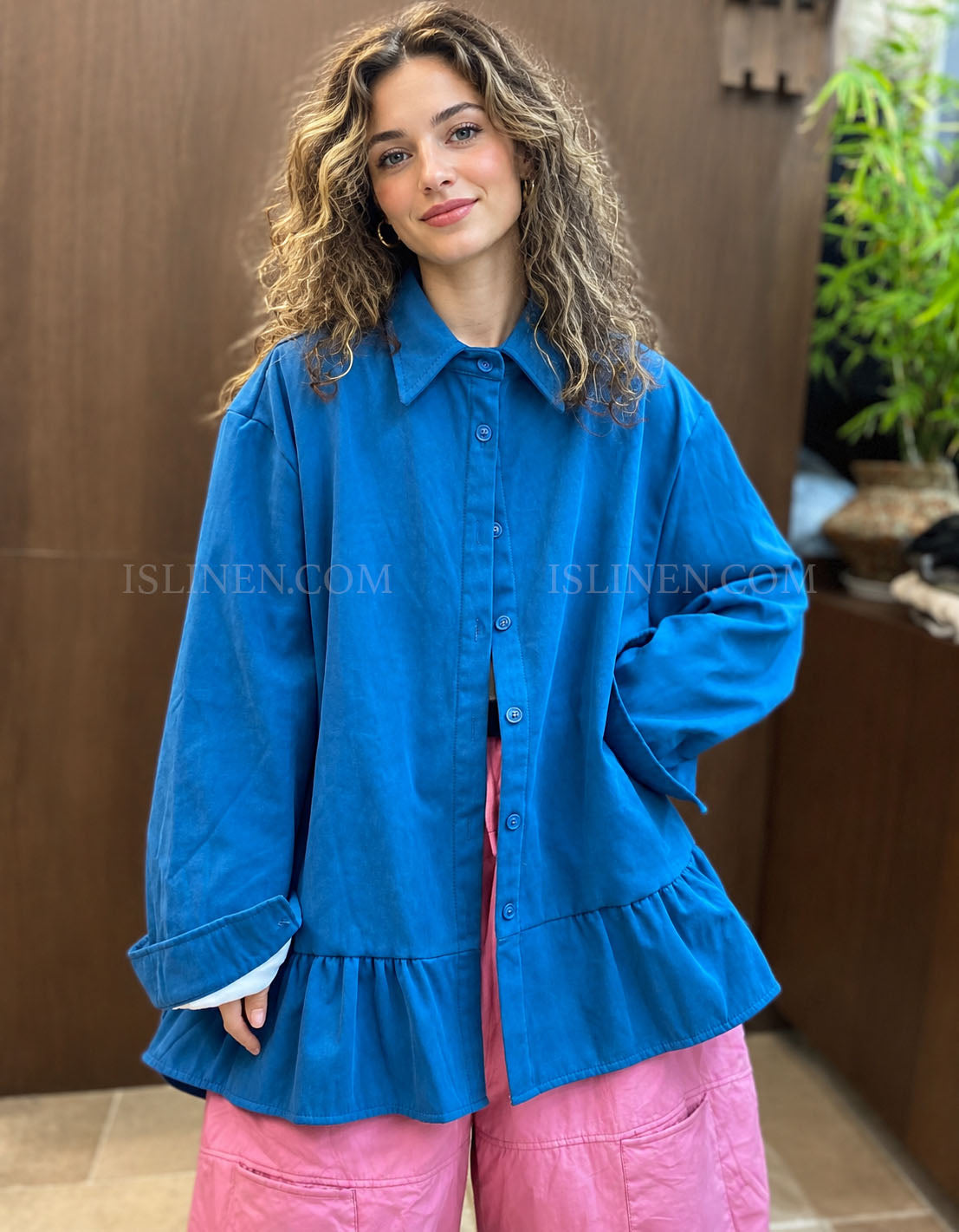 Woman wearing an oversized blue button-up shirt with a gathered ruffle hem, front view.