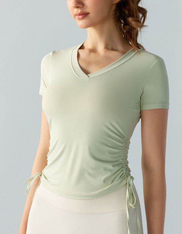 Woman wearing a light green ruched top against a gray background