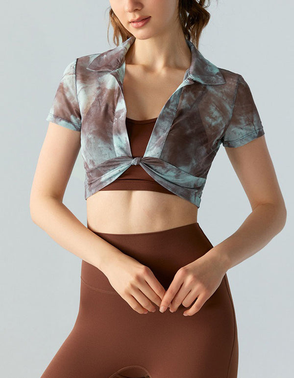 Woman wearing a patterned crop top and brown leggings on a plain background