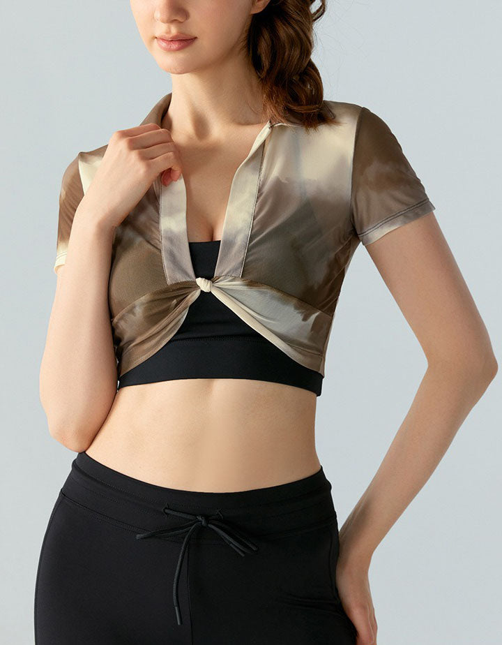 Woman wearing a black sports bra and leggings with a sheer gold top over a gray background