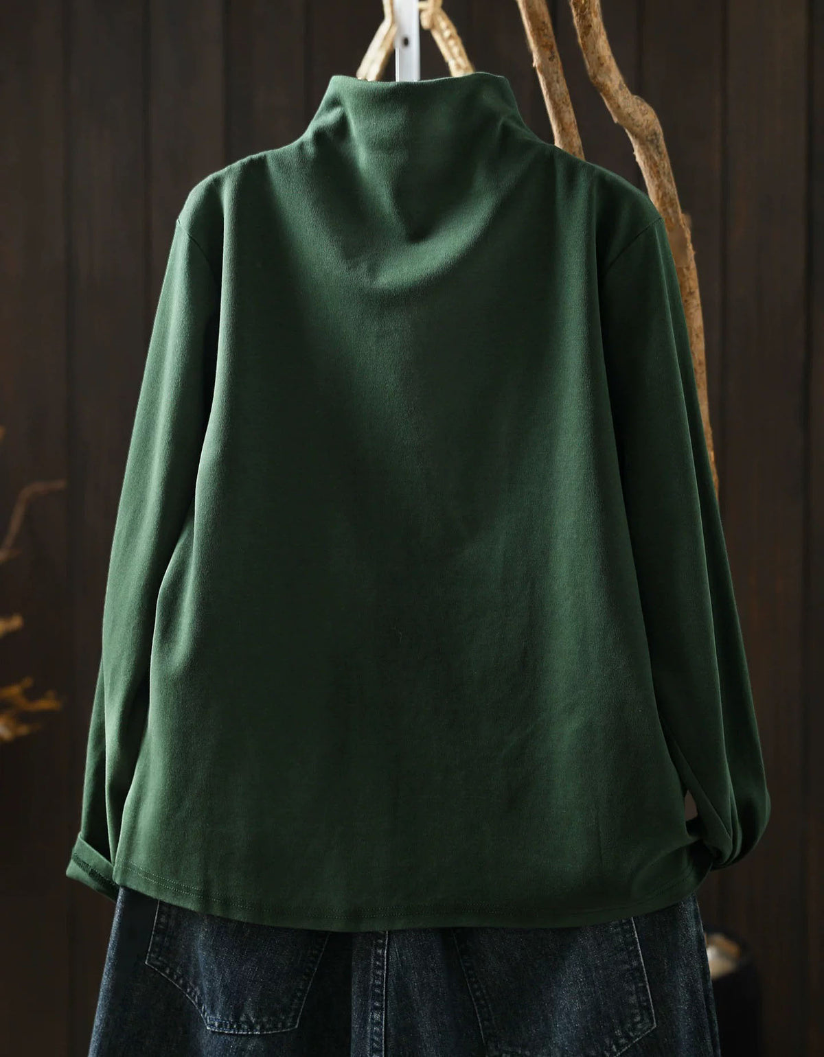 Back view of dark green women's high neck sweater with asymmetrical hem and side button detail