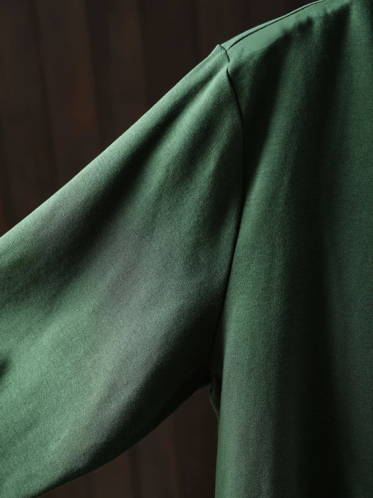 Decorative side button and asymmetrical hem detail on a forest green women's sweater