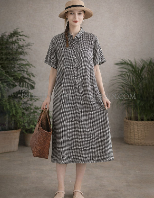 Woman wearing black gingham linen midi shirt dress with short sleeves, straw hat and woven tote bag, front view