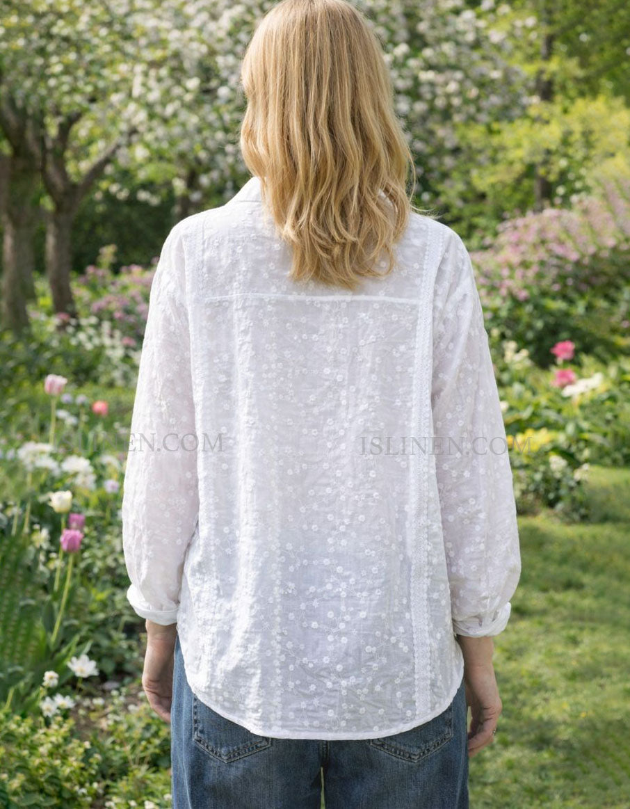 Person wearing a white blouse with floral patterns in a garden setting