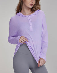 Woman wearing a purple long-sleeve top with a hood and gray leggings on a light gray background