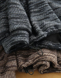 Close-up of folded striped knit fabric in dark charcoal gray and brown tones, showing the textured weave and drawstring details.