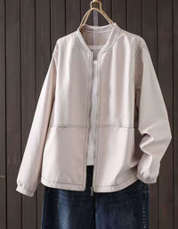 Beige faux leather bomber jacket with zip-up front hanging against a dark wood panel background