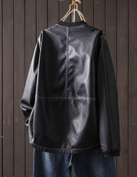 Black faux leather bomber jacket with zip-up front hanging against a dark wood panel background