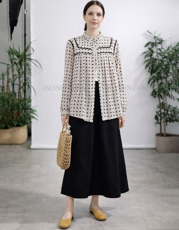 Woman wearing a patterned blouse and black skirt with yellow shoes, standing in a minimalistic room with plants.