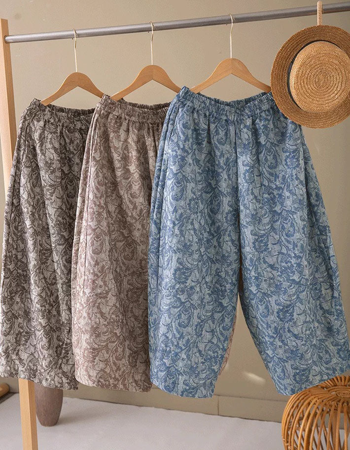 Three loose, patterned harem-style pants hang on wooden hangers from a clothing rack. 