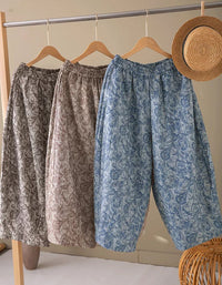 Three loose, patterned harem-style pants hang on wooden hangers from a clothing rack. 