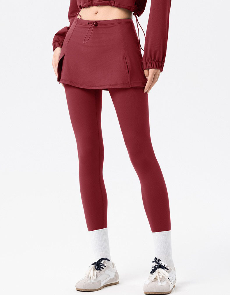 Person wearing a maroon outfit with a skirt and leggings on a white background
