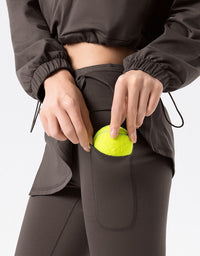 Person putting a green ball into a pocket of dark gray pants on a light gray background