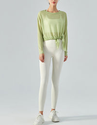 Person wearing a light green long-sleeve top and white leggings on a plain background