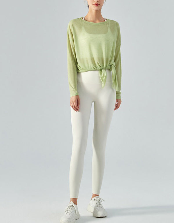 Person wearing a light green long-sleeve top and white leggings on a plain background