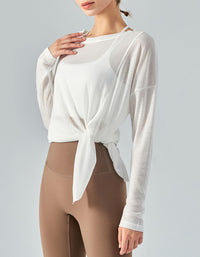 Woman wearing a white long-sleeve top with a knot detail and beige leggings on a gray background