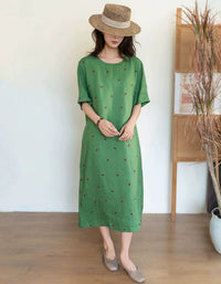 Woman wearing a green dress with small patterns and a straw hat indoors.