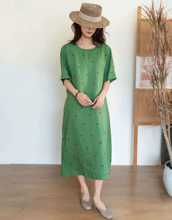 Woman wearing a green dress with small patterns and a straw hat indoors.