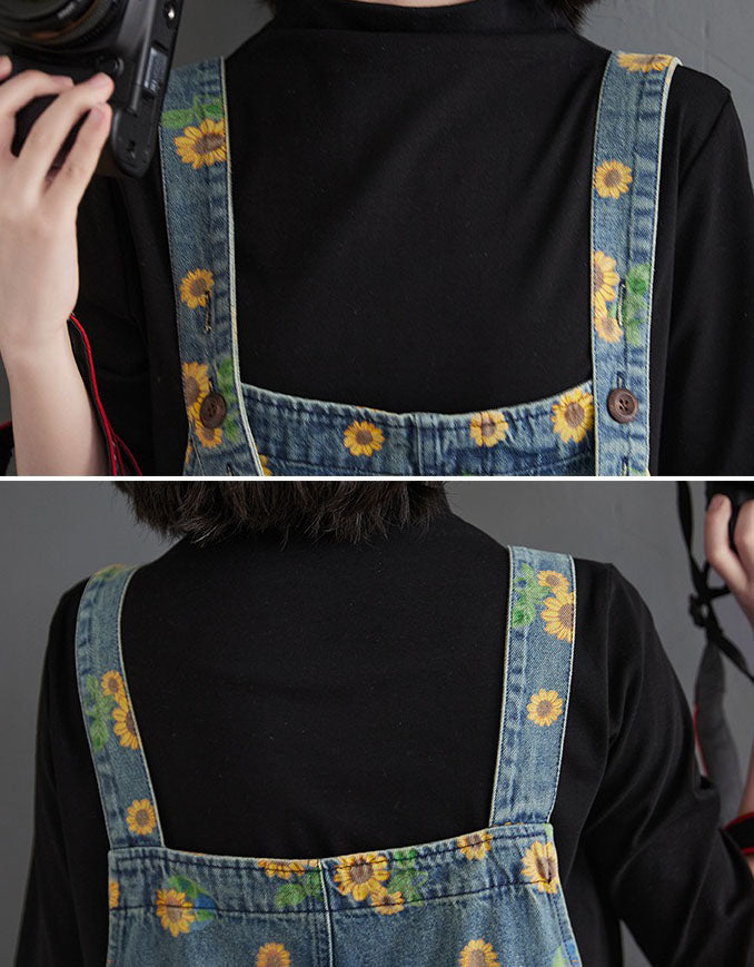 Person wearing a black top and denim overalls with sunflower patterns, holding a camera.