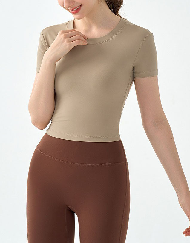 Woman wearing a beige athletic top and brown leggings on a light gray background