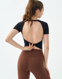 Woman wearing a black open-back top and brown leggings on a white background