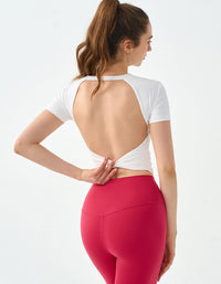 Woman wearing a white open-back top and red leggings on a light gray background