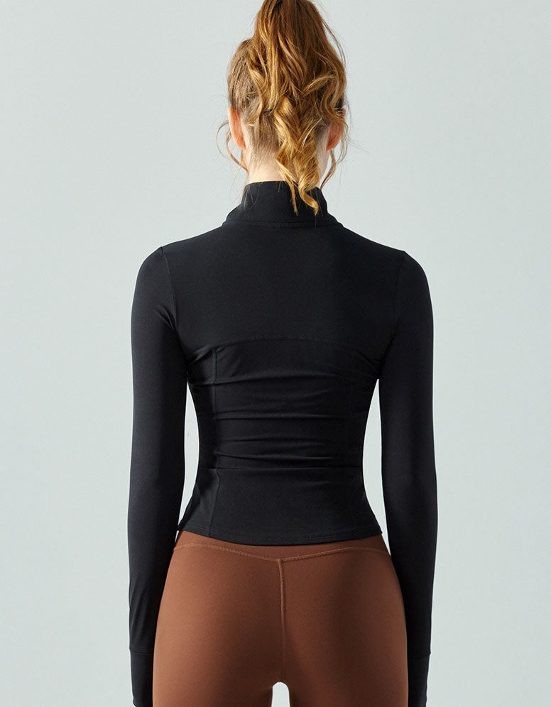 Person wearing a black long-sleeve top and brown leggings on a light gray background back view