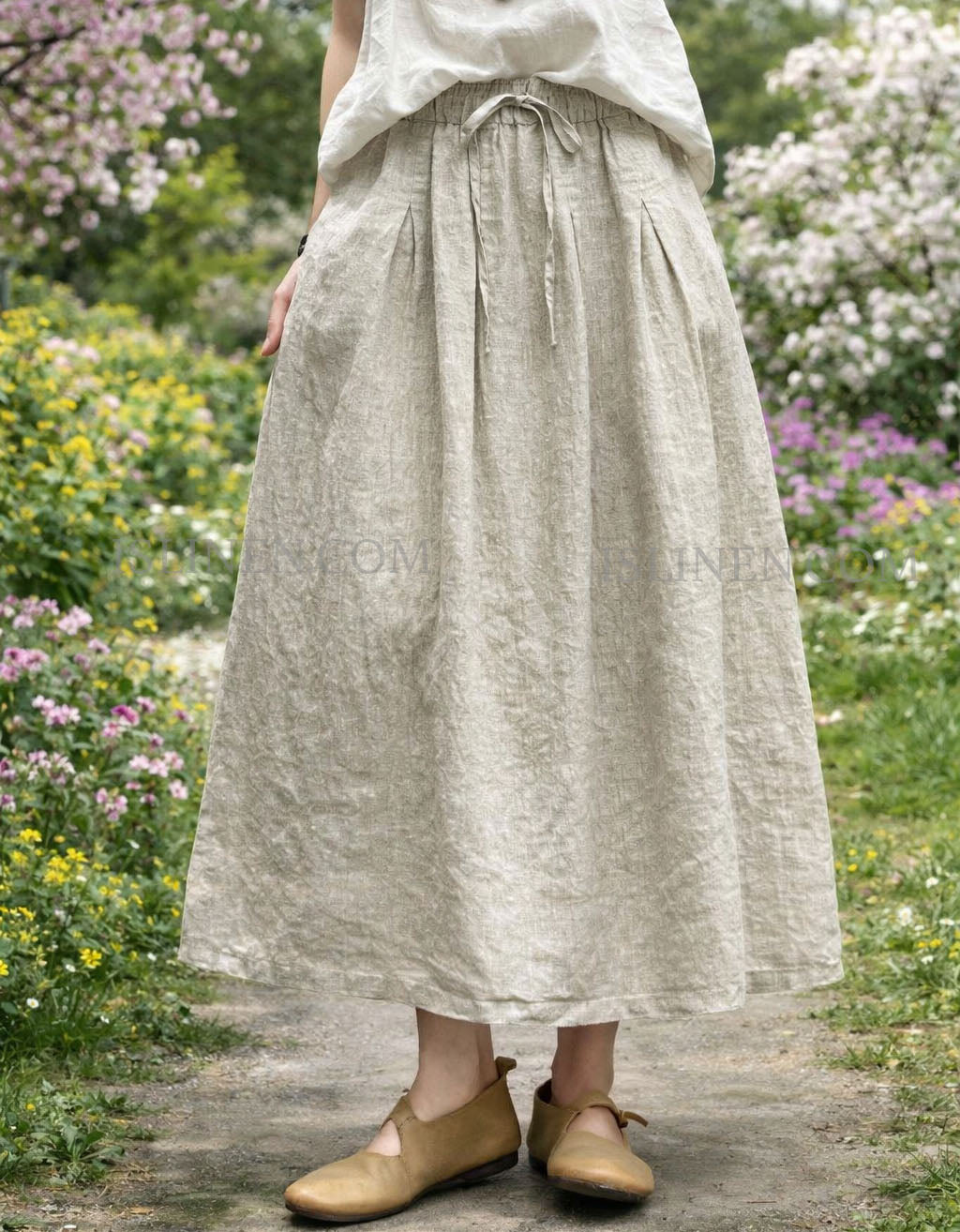 Woman wearing beige linen maxi skirt with pockets and elastic waist, styled with matching linen top in a garden path setting.