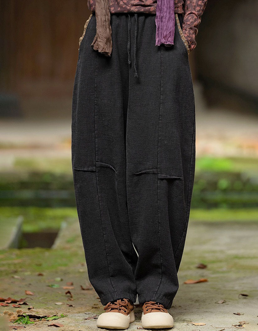 Black harem pants with a relaxed silhouette and rolled ankle cuffs, styled with brown casual shoes.