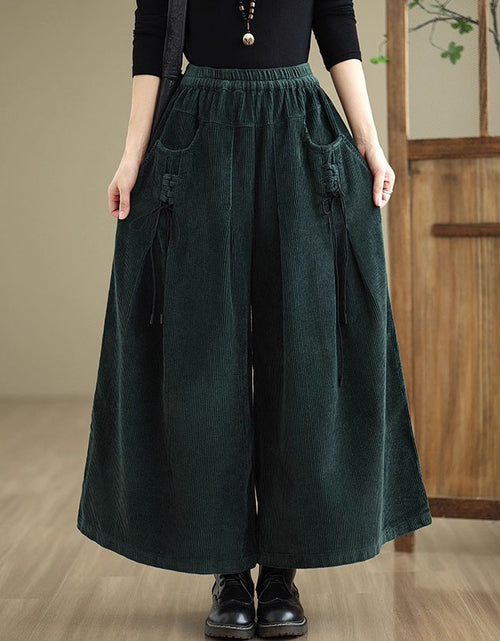 Person wearing dark green wide-leg pants with a wooden door in the background