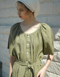 Woman wearing a green dress with a white headscarf against a stone wall.