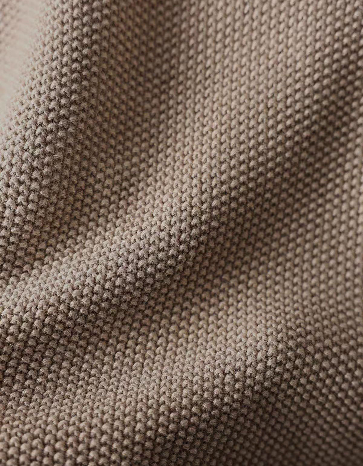 Close-up of a textured knit fabric in a warm taupe-beige color, showing the detailed weave and soft folds.