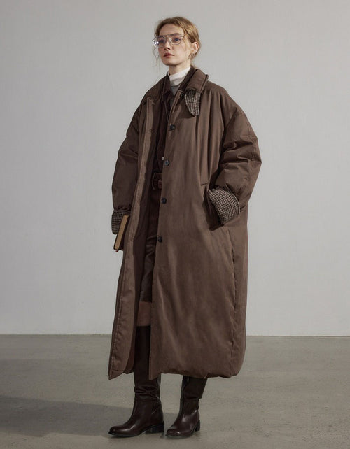 Person wearing a long brown coat against a plain background